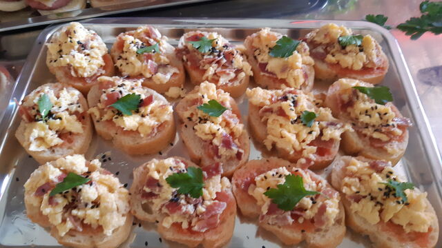 Tapa, sobre pan ligeramente tostado cama de tomate con ajo y aceite de oliva virgen, revuelto de jamon Serrano y hoja de pereji