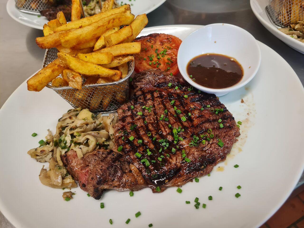 Entrecôte limousine cuite au char-grill , tomate rôtie , fricasse de pleurotes persillée, frites maison et son jus . 