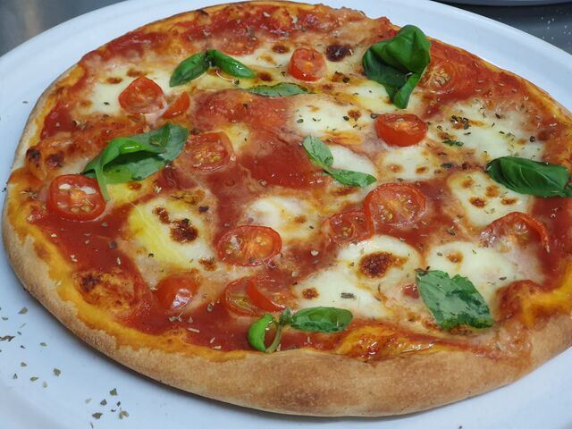 Pizza mit Mozzarella, Cherrytomaten und Basilikum mit Olivenöl verfeinert 
