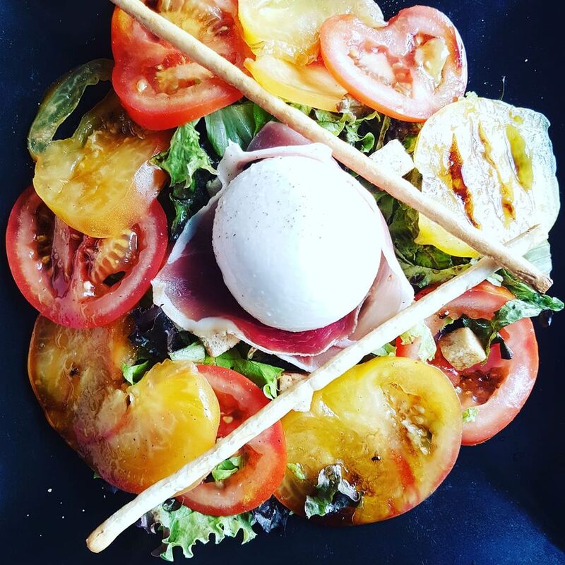 idée plat du jour : salade italienne avec tomates colorées, burratina, jambon cru de Parme sur un lit de salade verte. 