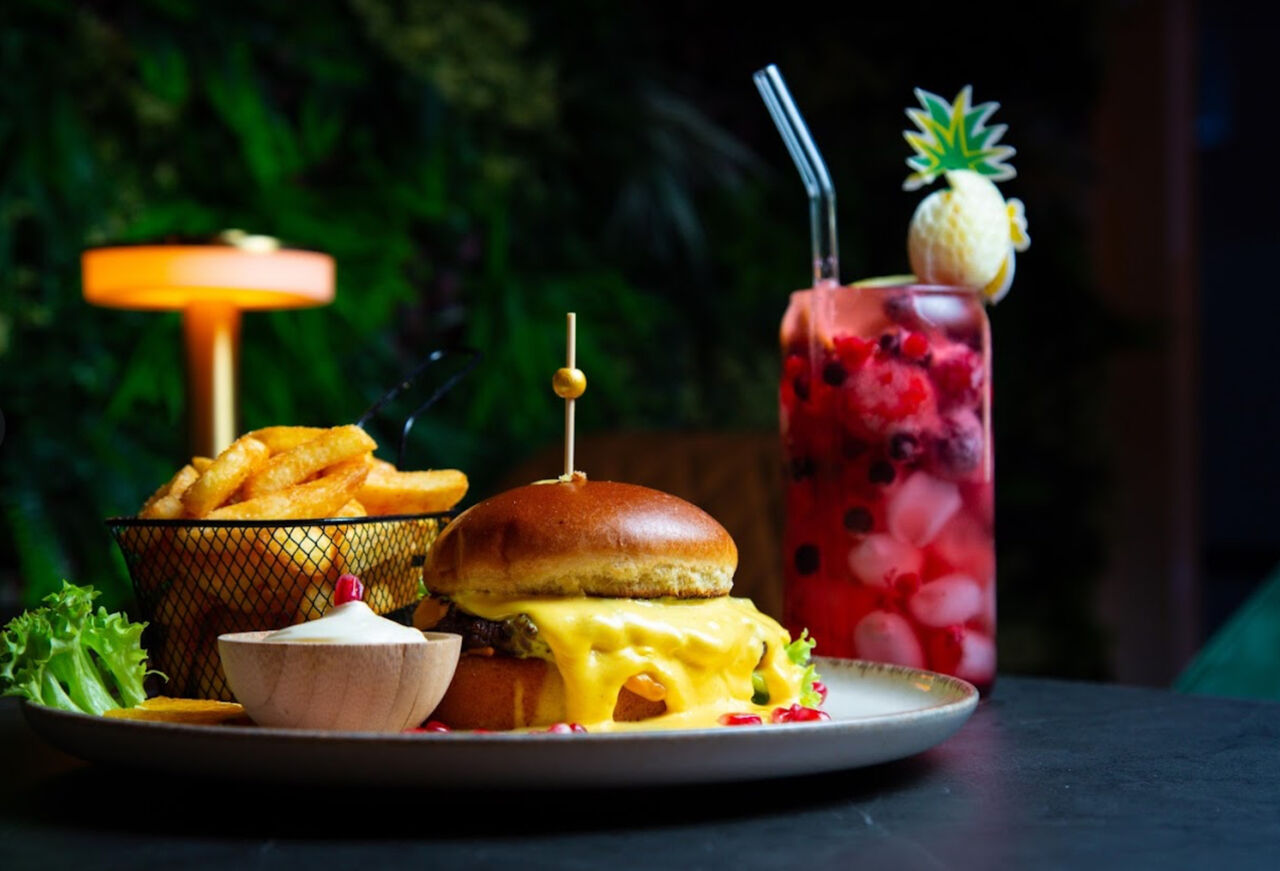 Ein Burger mit einem kalten Getränk, saftigem Fleisch und einer Beilage aus knusprigen Pommes