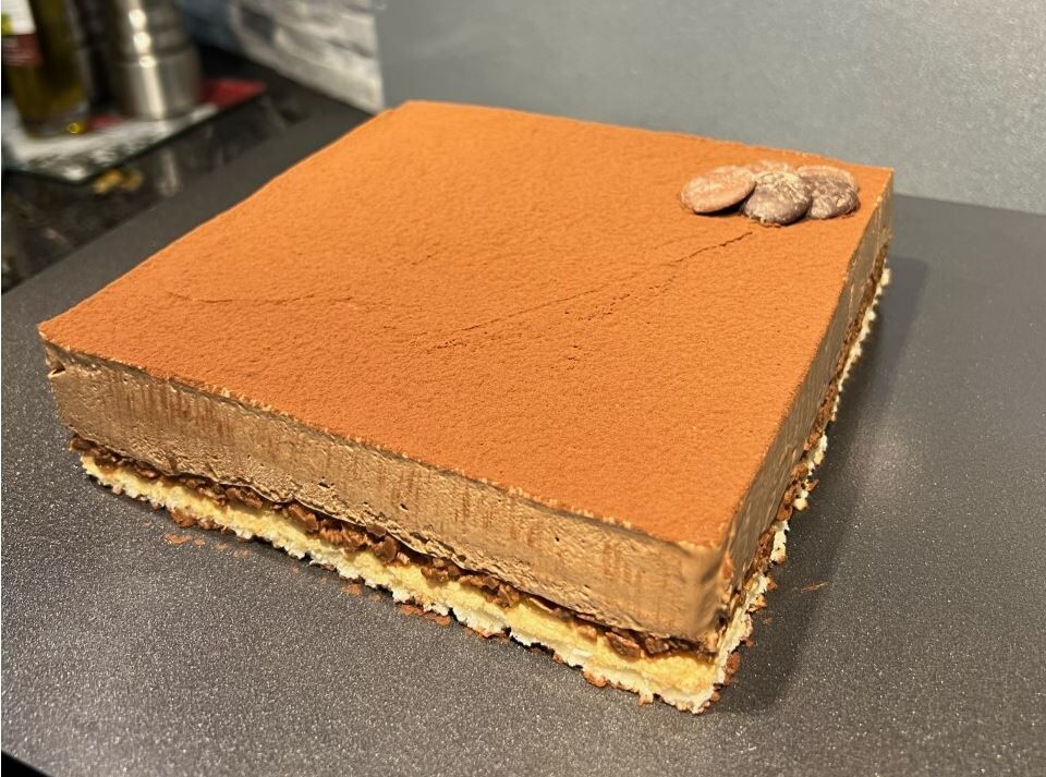 Gâteau Royal Chocolat avec sa dacquoise noix de coco, son croustillant praliné et sa mousse au chocolat noir saupoudré de cacao.