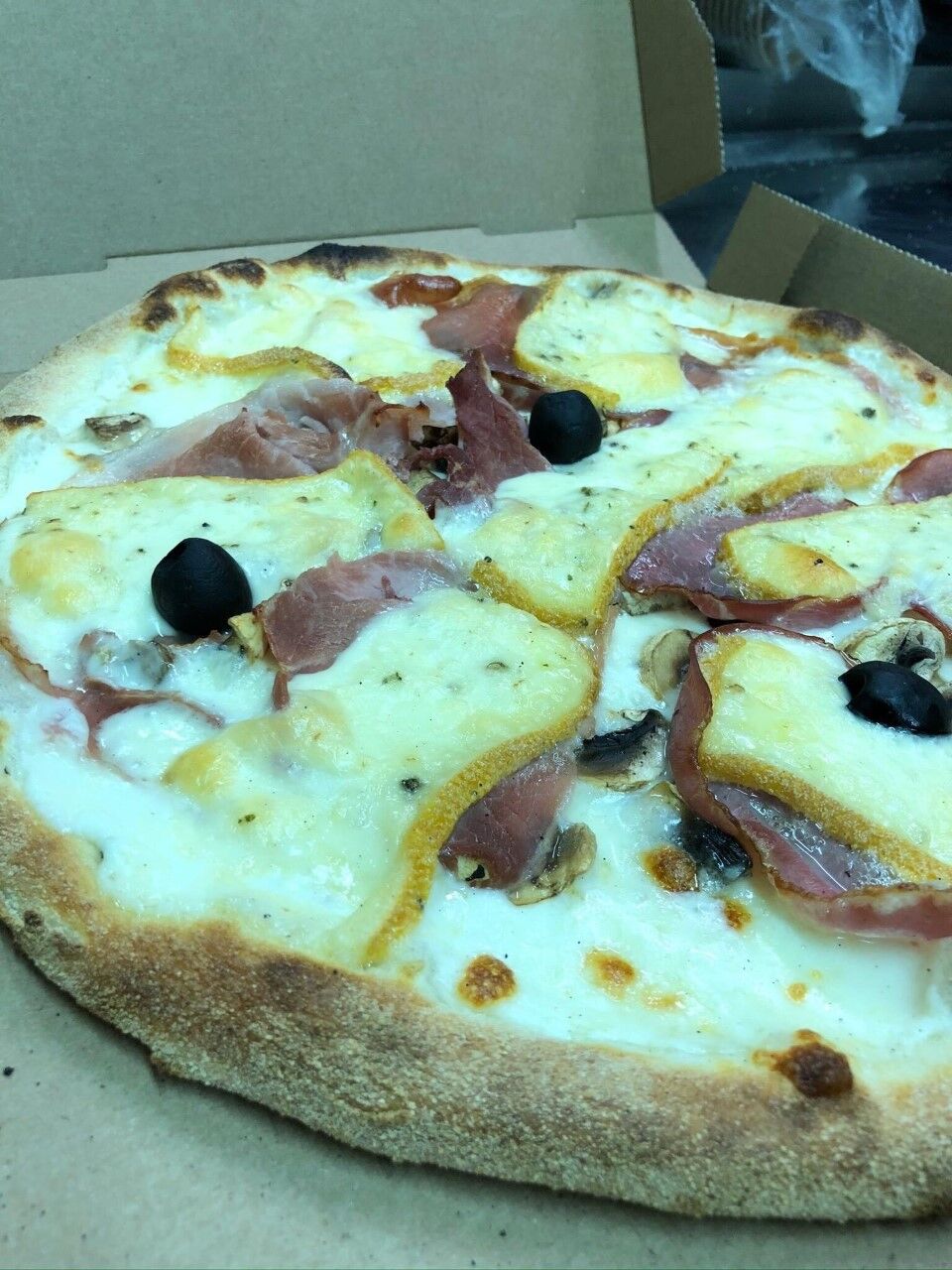 Pizza base crème, mozzarella, champignons, jambon blanc, jambon cru, bacon, raclette au poivre 