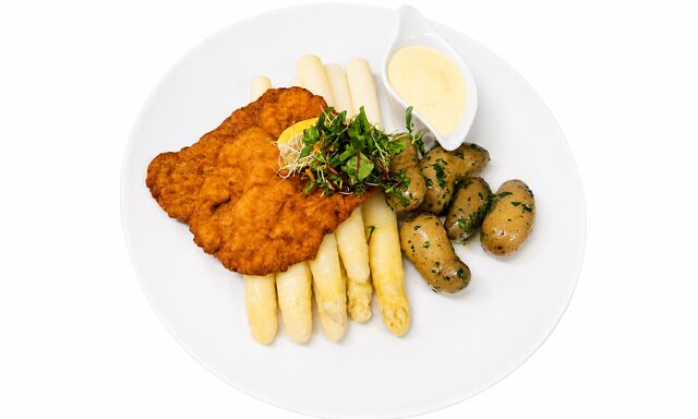 Portion frischer Stangenspargel mit Sauce Hollandaise, Petersilienkartoffeln und einem ausgebackenen Schnitzel