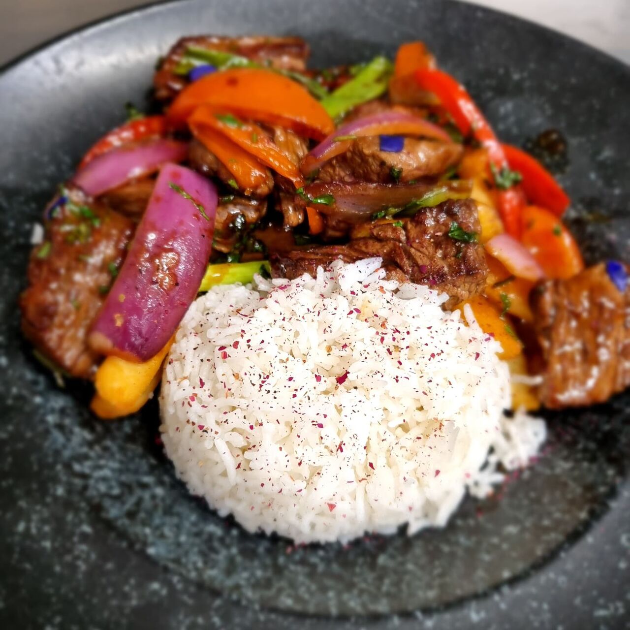 Lomo Saltado, bavette irlandaise flambée avec des légumes à sauce soja-huître. Accompagné de frites et Riz.