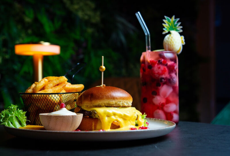 Ein Burger mit einem kalten Getränk, saftigem Fleisch und einer Beilage aus knusprigen Pommes