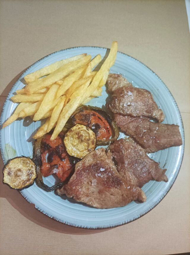 Presa con patatas fritas y guarnición de verduras.