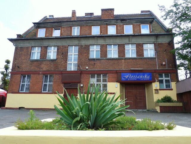 Widok z zewnątrz na budynek, parking i wejście główne.